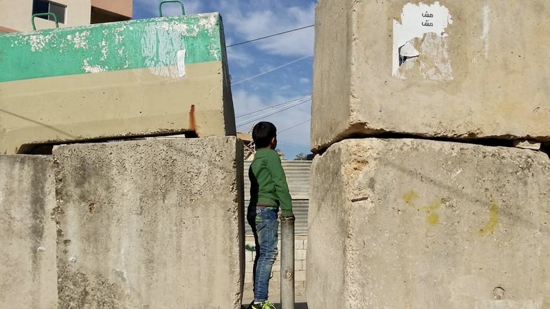 A child stands in a narrow opening between concrete blocks. The Lebanese army limits the passage of cars into a number of Palestinian camps through checkpoints and closes other entrances with concrete walls, leaving only pedestrian pathways. Burj al-Shemali camp, Tyre. January 21, 2017. (Nadia Ahmad/The Public Source)