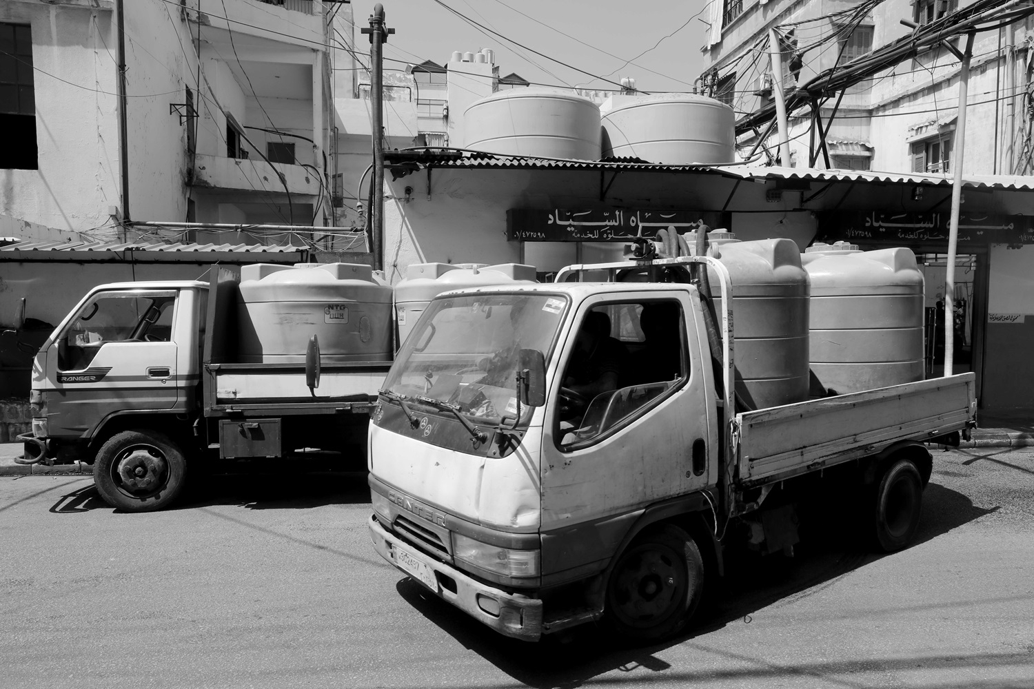 A pickup truck with plastic tanks loaded on its back is parked in front of a well called "al-Siyyad."