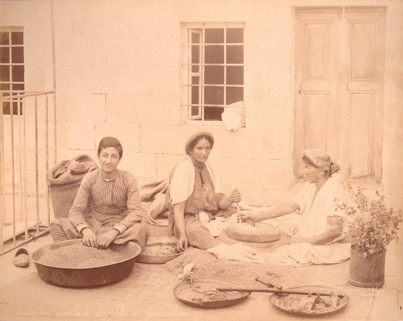 Two women, a boy, a pivotal grinding stone, wheat, and a scale with weights.