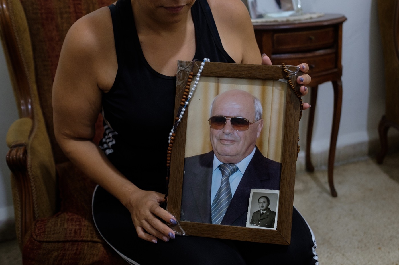 A photograph of a man in sunglasses is held by someone whose face is not shown in the photo.