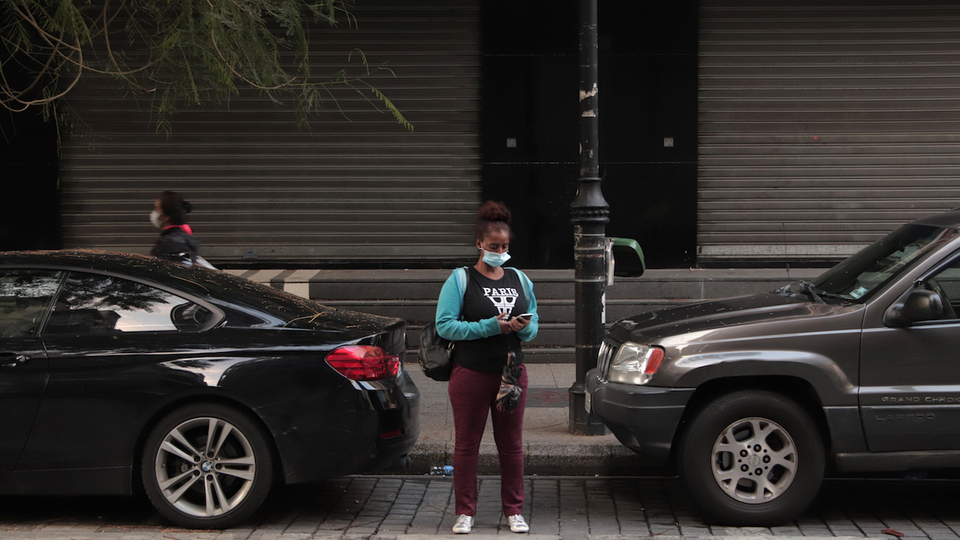 A woman waits for a taxi ahead of the 5 p.m. curfew along the shuttered Hamra Street in Beirut, Lebanon. November 27, 2020. (Fátima Fouad/The Public Source)